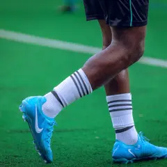 Piłkarz w turfy na zielonej murawie. Jasnoniebieskie buty piłkarskie Nike z białymi skarpetkami i czarnymi paskami.