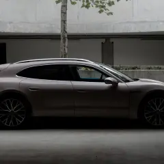 Elegancki Porsche Taycan 4S w kolorze piaskowym, zaparkowany w nowoczesnym garażu z betonowymi ścianami i drzewem.