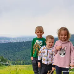 Trójka uśmiechniętych dzieci na tle górskiego krajobrazu z wyciągiem krzesełkowym. Idealne chełm atrakcje dla dzieci na wakacje.