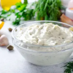 Una ciotola di cremosa salsa tartara, con capperi, limone, aglio e aneto sullo sfondo.