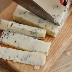 Un pezzo di gorgonzola viene affettato su un tagliere. Un desiderio di gorgonzola in gravidanza, magari per un aperitivo speciale.