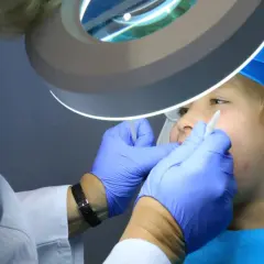 Dentysta w rękawiczkach bada usta dziecka pod lampą powiększającą.