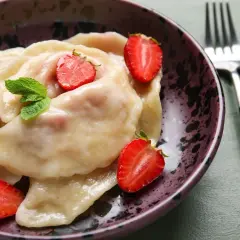 Pyszne pierogi z truskawkami, udekorowane świeżymi owocami i miętą, w ozdobnej misce.
