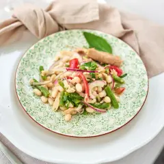 Ein bunter Thunfisch-Bohnen-Salat, italienisch inspiriert, mit grünen Bohnen, roten Zwiebeln und Tomaten auf einem Teller mit grünem Muster.