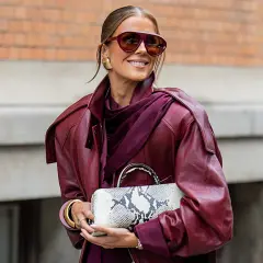 Kobieta w bordowej ramonesce i okularach przeciwsłonecznych prezentuje modne stylizacje na wiosnę, trzymając w ręku torebkę w wężowy wzór.