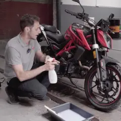 Uomo con spray e secchio di schiuma, pronto a usare prodotti casalinghi per lavare moto.