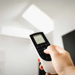 Main tenant ajuste la température de son climatiseur PAC split à 21°C avec la télécommande.