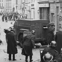 Unruhen in Nordirland, ein gepanzertes Fahrzeug und Polizisten mit Schilden. Die Szene erinnert an die Zeit vor dem Karfreitagsabkommen.