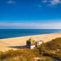 Piękna plaża i morze, idealne na spacer po jednej z **miejscowości nad morzem koło Gdańska**. W oddali widać charakterystyczny budynek.