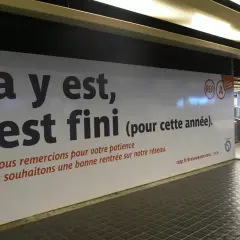 Panneau RATP annonçant la fin des travaux sur le RER A. Une personne en fauteuil roulant passe devant.