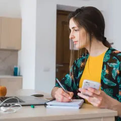 Kobieta pracuje przy laptopie, notując i sprawdzając telefon. Zastanawia się, jak obliczyć czynsz za niepełny miesiąc.