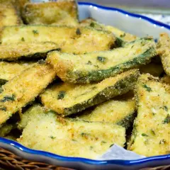 Fettine dorate di zucchine in padella, croccanti e saporite, servite in un piatto blu bordato.