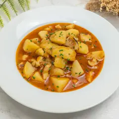Plato de patatas con sepia, un guiso casero que evoca las patatas con sepia de la abuela, con trozos de patata y sepia en una salsa rojiza.