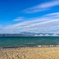 Spokojne morze i plaża w Grecji w styczniu. W oddali widać most i góry.