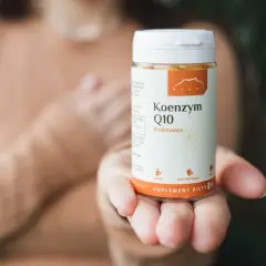 Dłoń trzyma buteleczkę suplementu diety z koenzymem Q10.