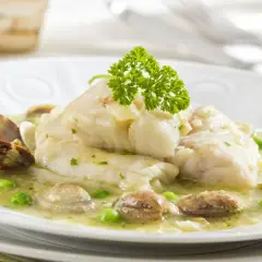 Merluza en salsa verde con almejas y guisantes, decorada con perejil fresco. Un plato marinero delicioso.