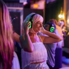 Uśmiechnięta kobieta z blond włosami cieszy się imprezą w stylu silent disco, zakładając świecące na zielono słuchawki.
