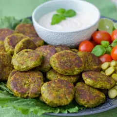 En tallrik med gyllene vegetariska biffar, serverade med en krämig dipp, körsbärstomater, gurkskivor och limeklyftor.