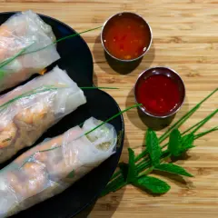 Tres rollitos de verano frescos con camarones y verduras, servidos en un plato negro con dos salsas y hojas de menta.