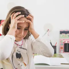 Zmartwiona dziewczynka z rękami na głowie. Jak rozładować stres u dziecka? Może przerwa od nauki?
