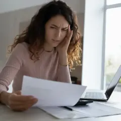 Zmartwiona kobieta z bólem głowy analizuje dokumenty, być może dotyczące odrzucenia spadku po bracie.
