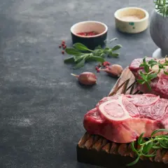 Deux grosses pièces de viande au barbecue, prêtes à être grillées, avec des herbes fraîches et de l'ail.