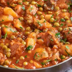 Un saporito spezzatino di vitello con piselli e patate, cotto in un sugo rosso e guarnito con prezzemolo fresco.