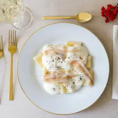 Piatto di paccheri conditi con una cremosa spuma di pecorino e guarniti con pepe nero. Accanto, posate dorate e un rametto di bacche rosse.