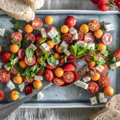 Frischer Tomate Mozzarella Salat mit bunten Kirschtomaten, Feta und Minze, serviert auf einem grauen Teller mit Brot.