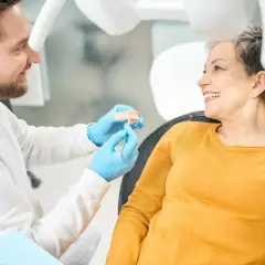 Dentista mostra un modello di denti a una paziente sorridente, discutendo di impianti dentali per un sorriso perfetto.