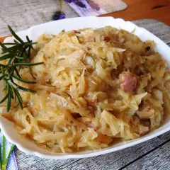 Pyszna kapusta zasmażana z boczkiem, podana na białym talerzu, ozdobiona gałązką rozmarynu.