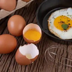 Œufs bruns sur table en bois, un œuf au plat dans une poêle. Le cholestérol des 2 œufs par jour est un sujet de débat.