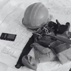 Kask, rękawice, młotek i kalkulator na planach budowlanych.