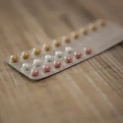 Opakowanie tabletek antykoncepcyjnych z kilkoma rzędami tabletek w różnych kolorach, leżące na drewnianym blacie.
