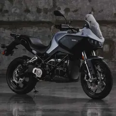 Motocicleta eléctrica Zero DSR/X, con potencia de 35kW, color gris oscuro, sobre suelo mojado y fondo de pared de ladrillo.