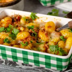 Zapiekane gnocchi z pomidorami i mozzarellą, posypane świeżą natką pietruszki, w zielono-białej kratce. Pyszne danie gotowe do podania.