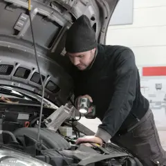 Mechanik z latarką bada silnik, szukając problemu z przegubem.