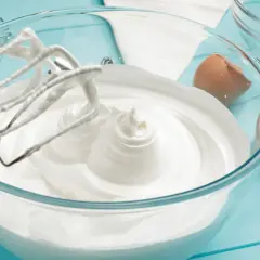 Ubity krem śmietankowy do tortu bez mascarpone, przygotowany z białek i cukru, w szklanej misie. Obok skorupki jajka.