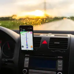 Telefon z nawigacją na desce rozdzielczej, pokazujący trasę. Czy Yanosik działa za granicą? Słońce zachodzi, droga przed nami.
