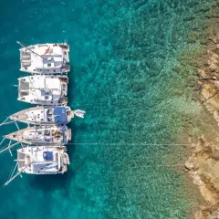 Flott bild av flera segelbåtar som ligger för ankar i turkost vatten nära en klippig kust. En dröm om att segla i Kroatien.