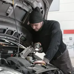 Mechanik samochodowy z latarką bada silnik. Zastanawiasz się, ile zarabia elektronik samochodowy?