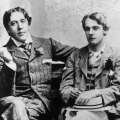 Oscar Wilde, lord elegancji i błyskotliwy pisarz, siedzi z młodym mężczyzną, trzymając papierosa.