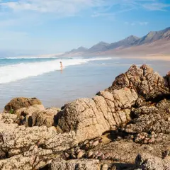 Una persona disfruta de las playas nudistas de Cantabria, con olas rompiendo en la costa y montañas al fondo.