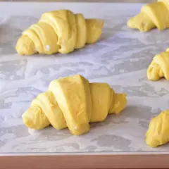 Cornetti fatti in casa, ancora crudi, disposti su una teglia foderata di carta forno, pronti per lievitare e diventare dorati.