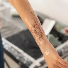 Un bras orné d'un tatouage floral délicat, la peau légèrement humide, comme si elle commençait à peler après la séance.