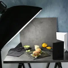 A food photography setup with burgers, salad, and a yellow pepper, illuminated by a large softbox, showcasing effective diy photography lighting.