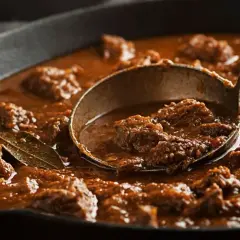 Gęsty, aromatyczny gulasz wołowy w żeliwnej patelni, z chochlą pełną mięsa. Idealny przykład, jak zagęścić sos, by był aksamitny.