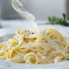 En krämig portion pasta alfredo med ånga som stiger, toppad med riven parmesan och svartpeppar.