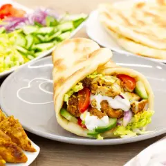 Pyszna shoarma drobiowa w picie z warzywami i sosem. Obok talerz z dodatkami: sałatka, pomidory, ogórki, cebula i placki chleba.