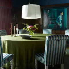 A dining room with a round green table, striped chairs, and a large painting. The table styles are classic and elegant.